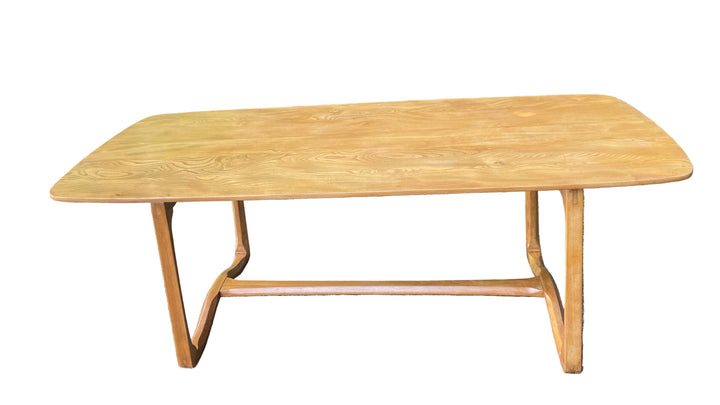 light oak dining table with rounded corners and a natural wood grain finish, photographed outdoors on grass with a green hedge in the background.