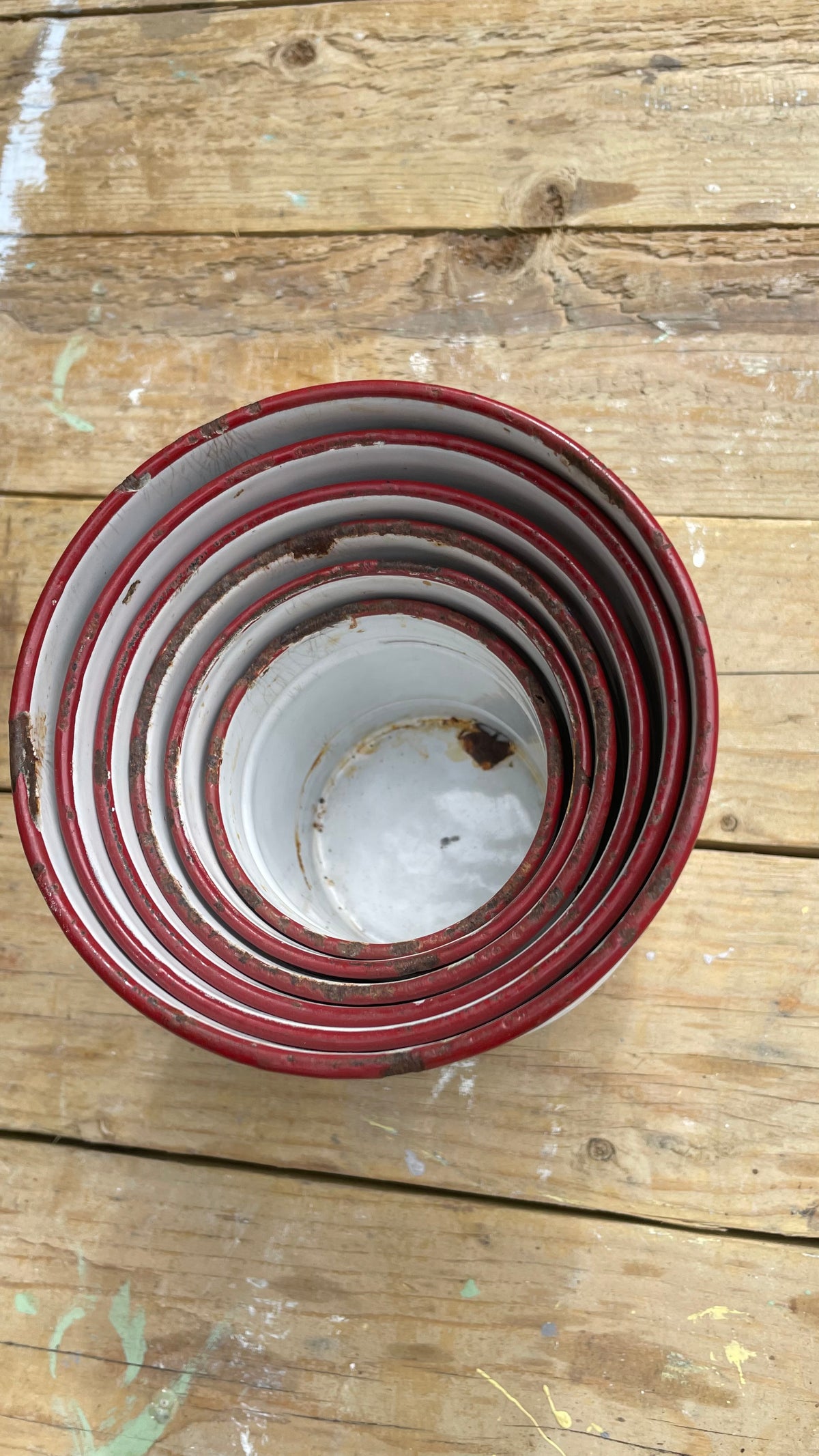 stack of nested round metal buckets or pails with red rims and white interiors, photographed from above on a rustic wooden plank surface.
Details