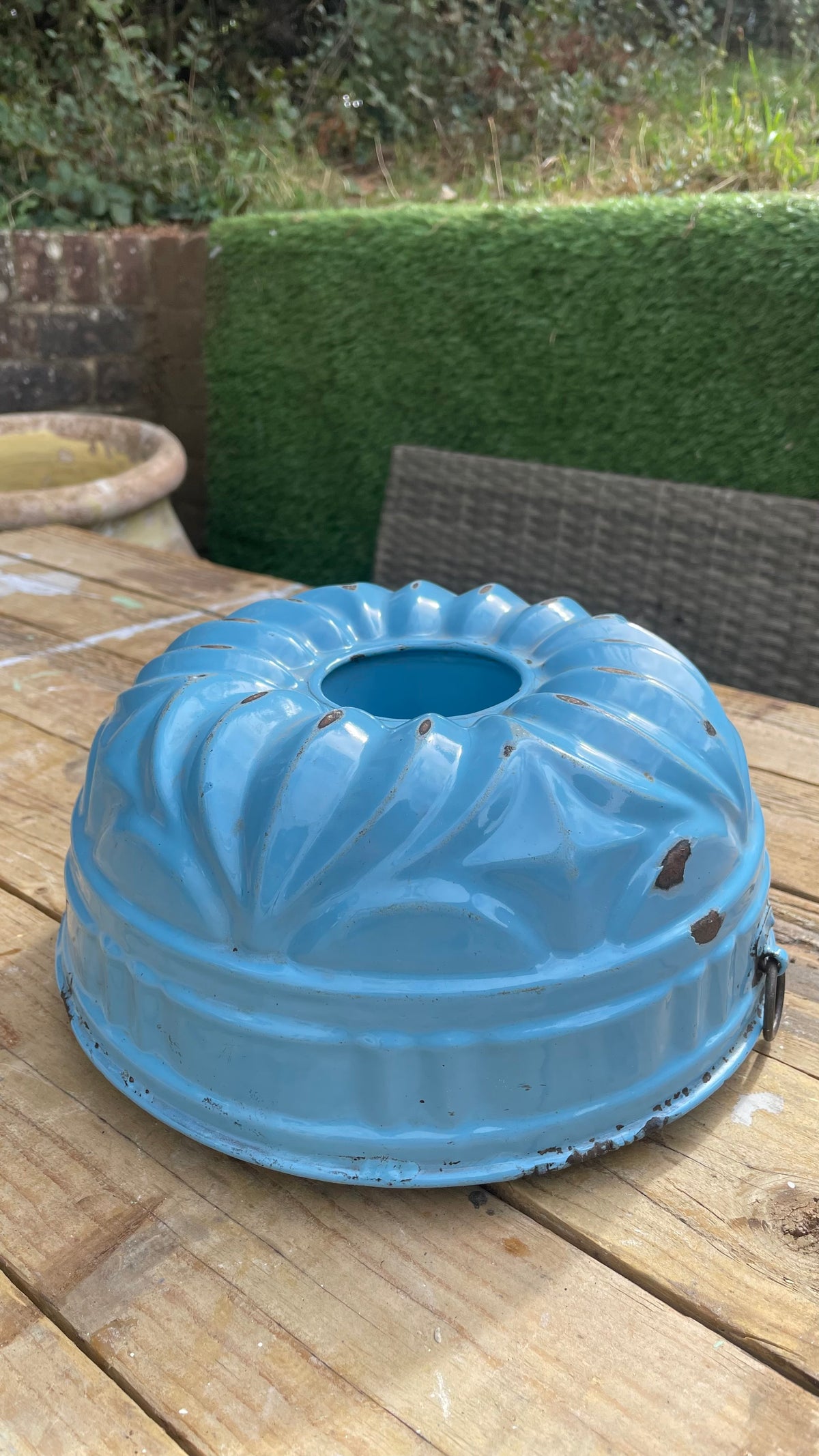 light blue vintage metal bundt cake pan with a fluted pattern, resting on a wooden deck table outdoors.
Details