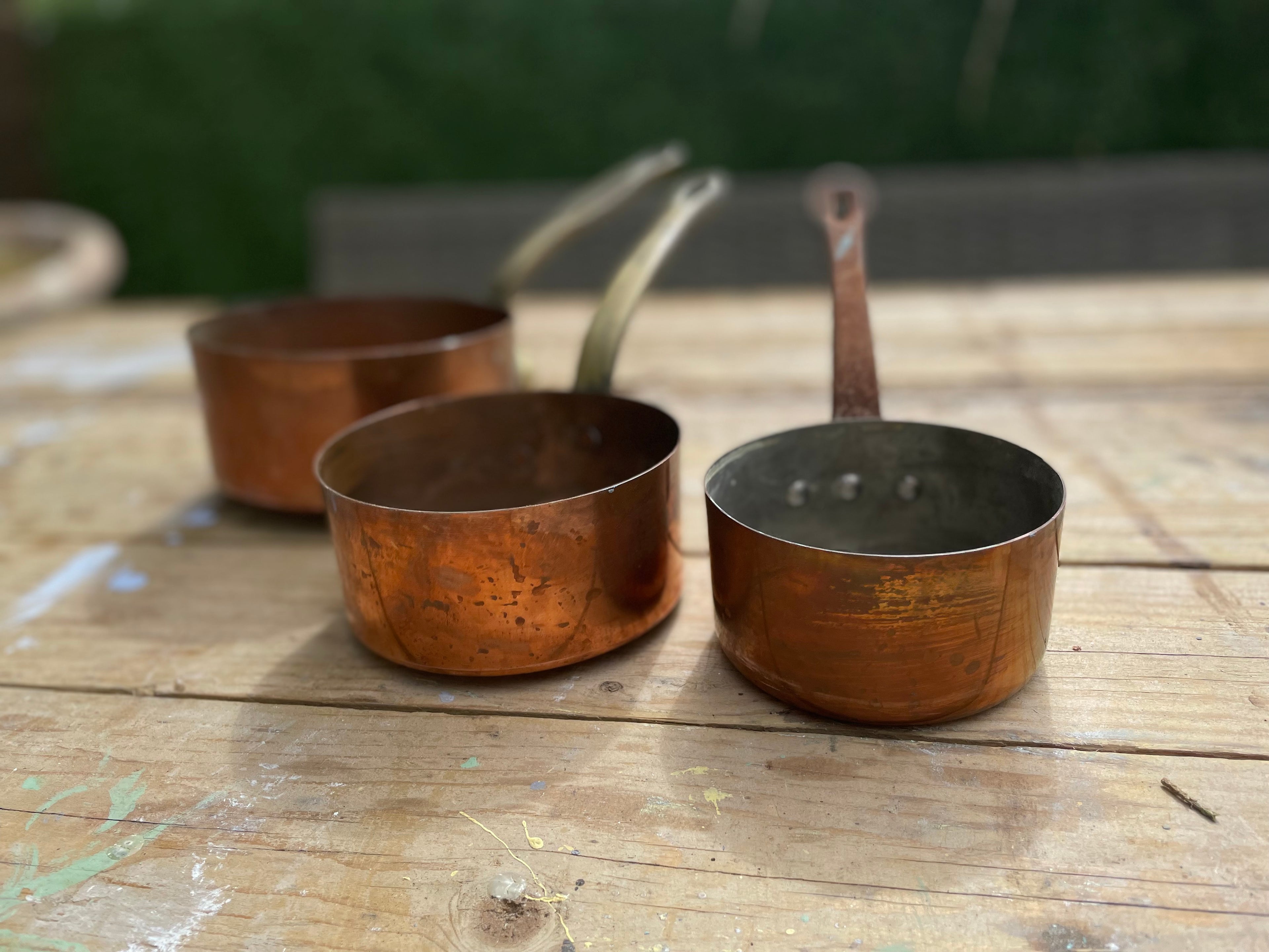 Three small copper saucepans with long handles resting on a rustic wooden table.
Details