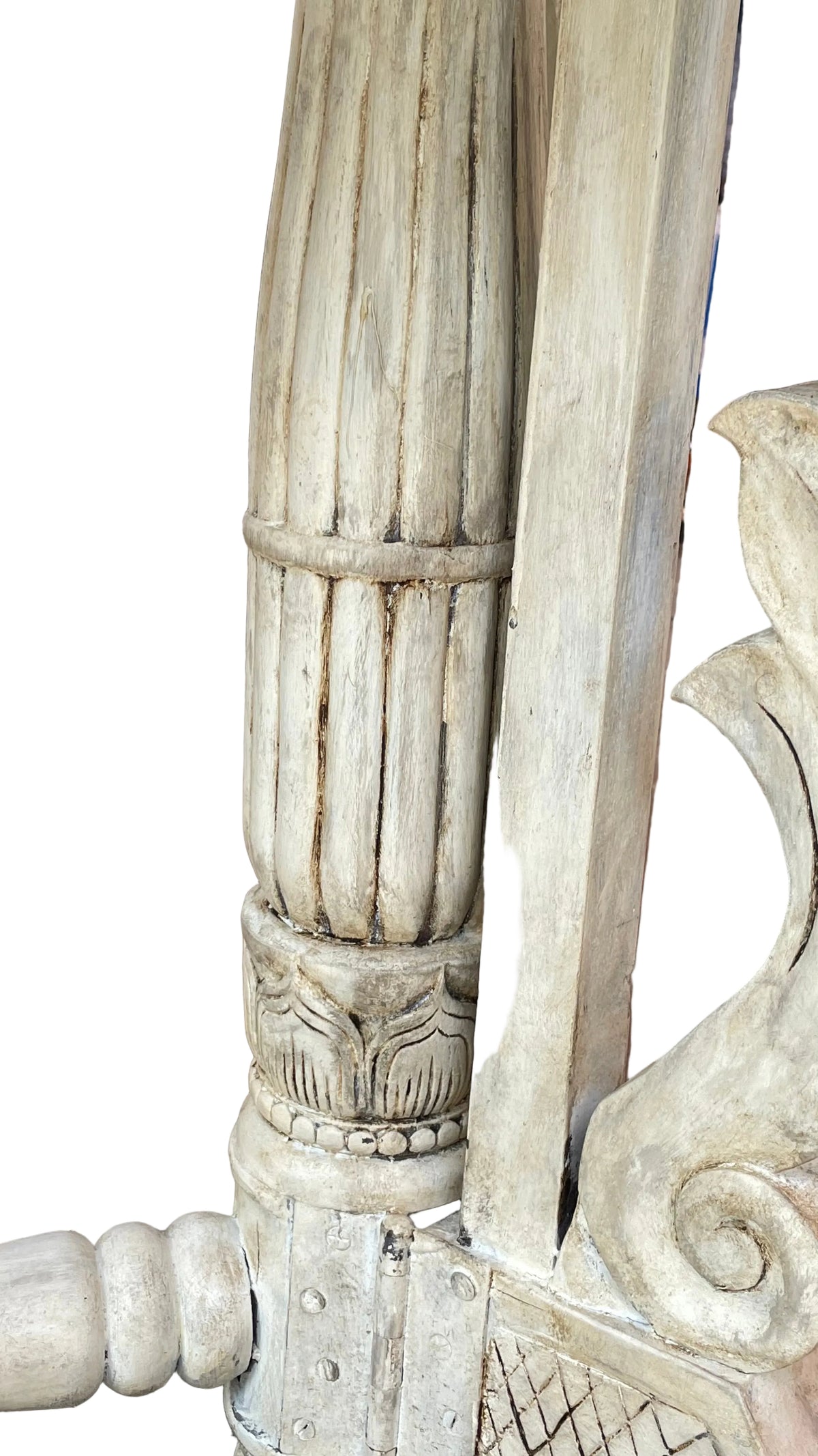 A close-up of a distressed, whitewashed wooden outdoor furniture frame, showing carved details and weathered wood grain on a concrete patio
