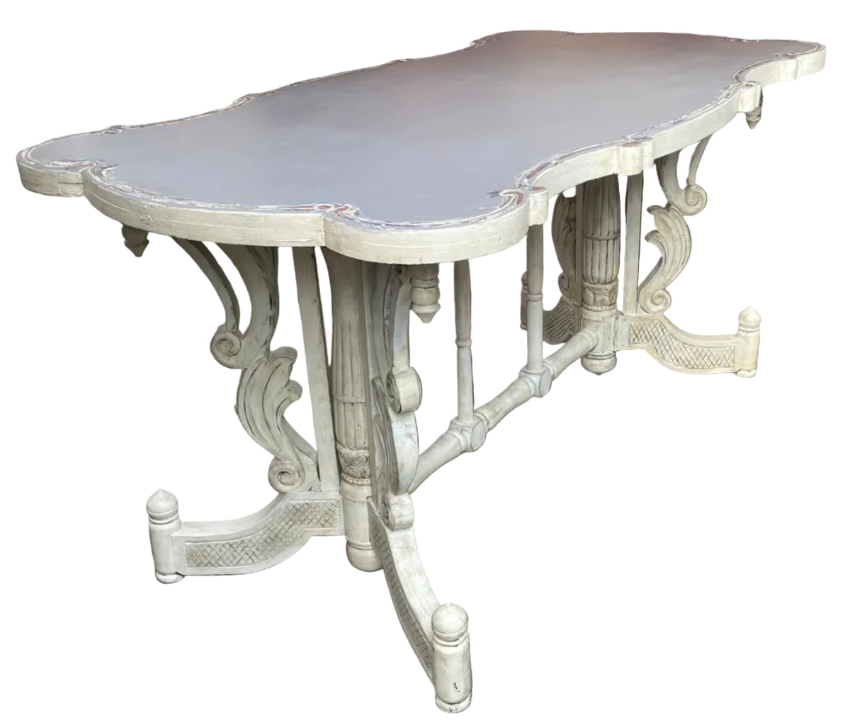 A distressed white carved wooden dining table with a scalloped top