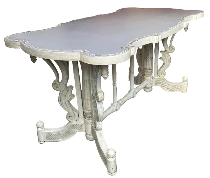 A distressed white carved wooden dining table with a scalloped top