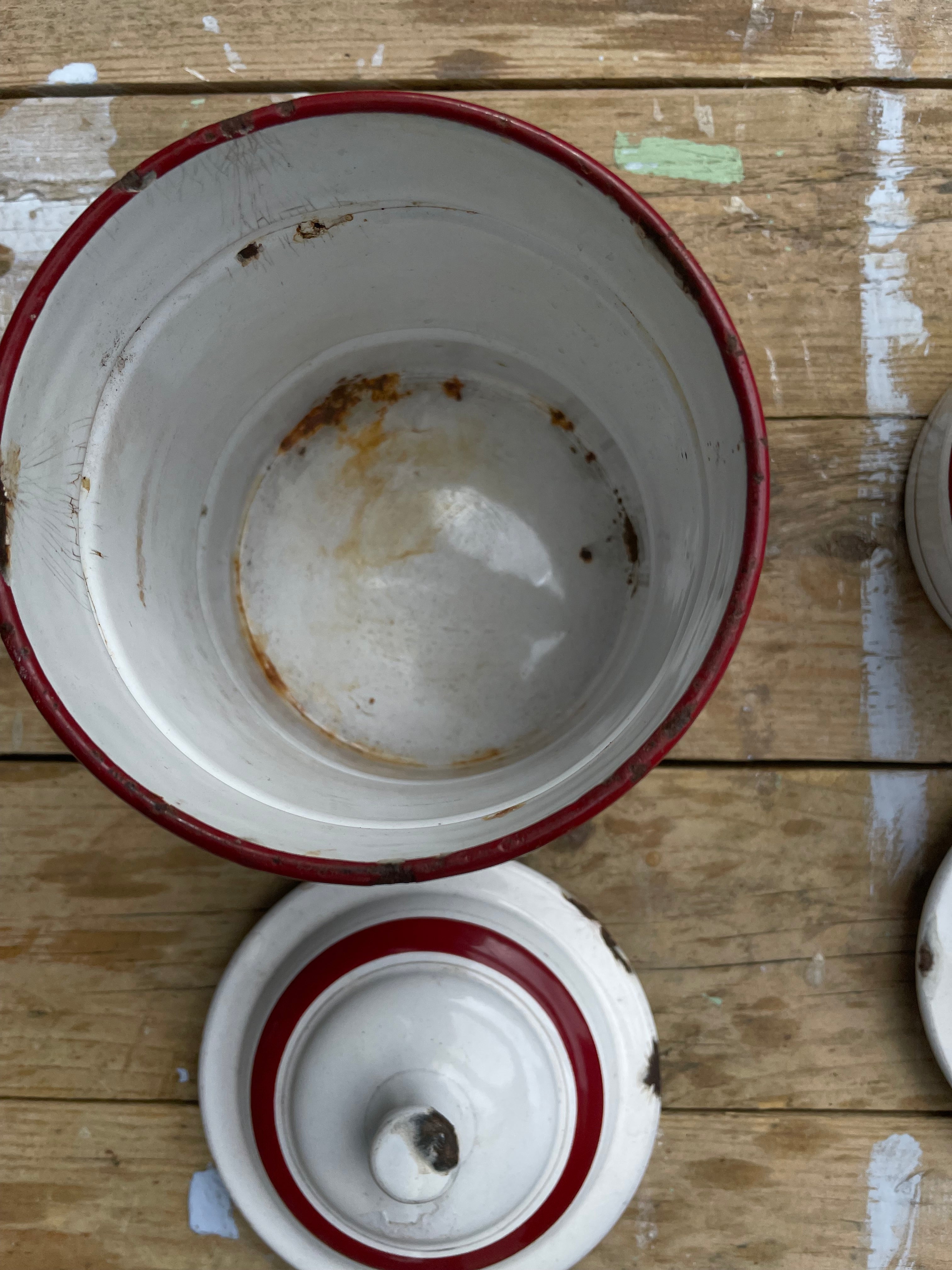 A vintage white enamel lidded jar with a red rim, shown open with the lid placed below on a rustic wooden plank surface.
Details
