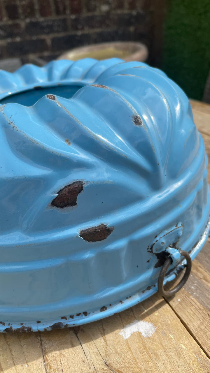 light blue enamel bandanna or headband with a scalloped edge and a metal ring pull, shown on a wooden surface with a blurred outdoor background.