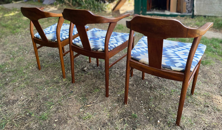 Three mid-century modern wooden dining chairs with blue and white patterned seat cushions, shown outdoors on a grassy lawn.