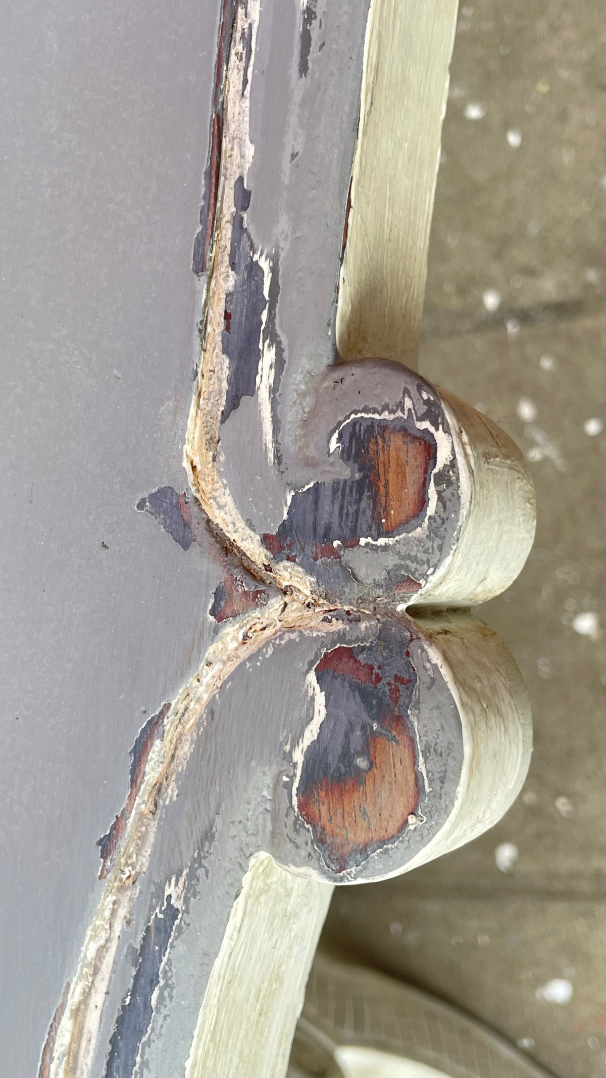 


A close-up of a distressed painted wooden frame corner, showing peeling gray and beige paint with exposed brown wood underneath.