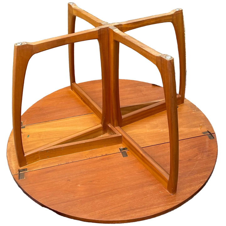 round wooden table base or pedestal with four upright support arms, photographed outdoors on a gray sheet with grass and shrubs in the background.