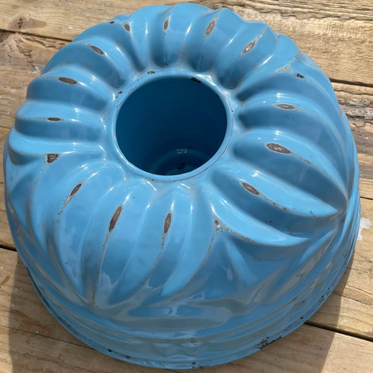 A light blue ceramic bundt-style pot with a ribbed exterior and a central hole, shown on a weathered wooden plank surface.
Details