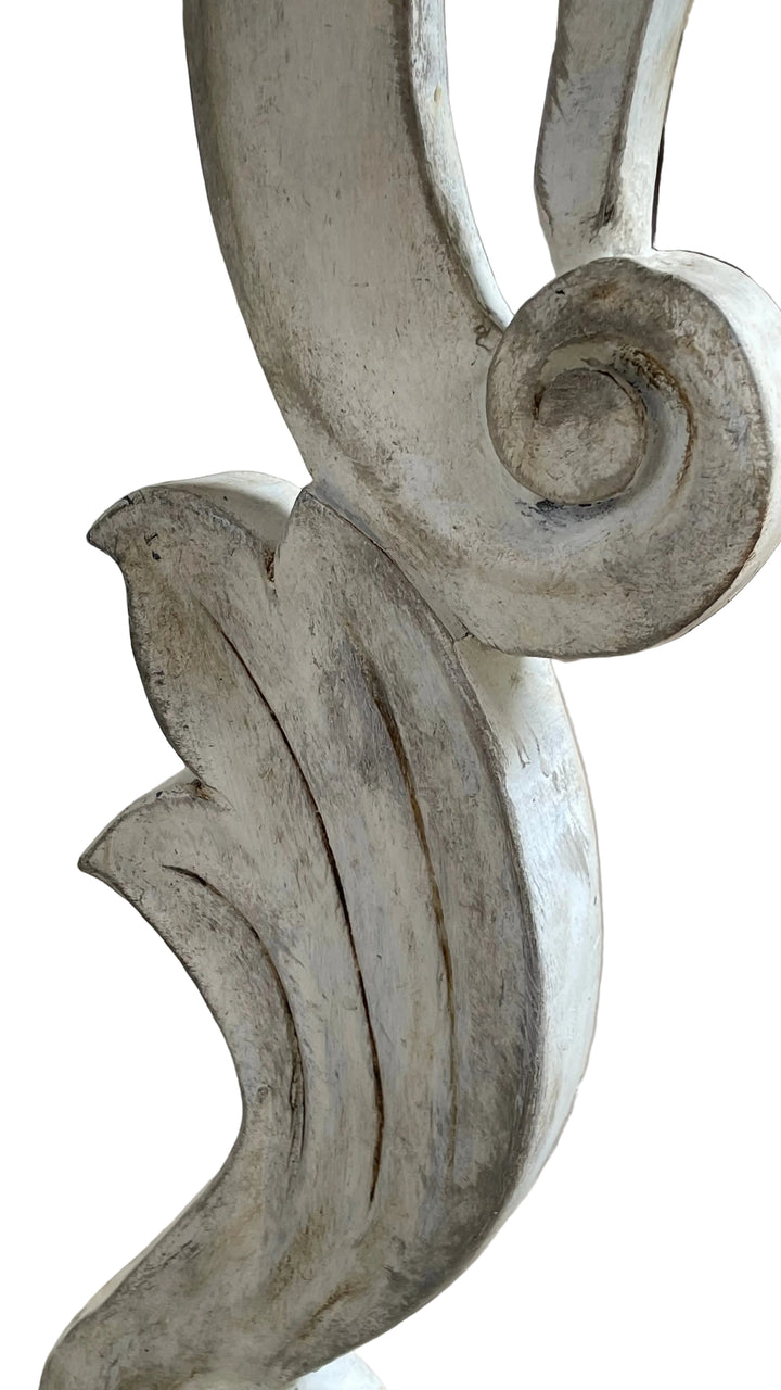 Close-up of a distressed white carved wooden decorative piece with scrollwork and leaf-like curves