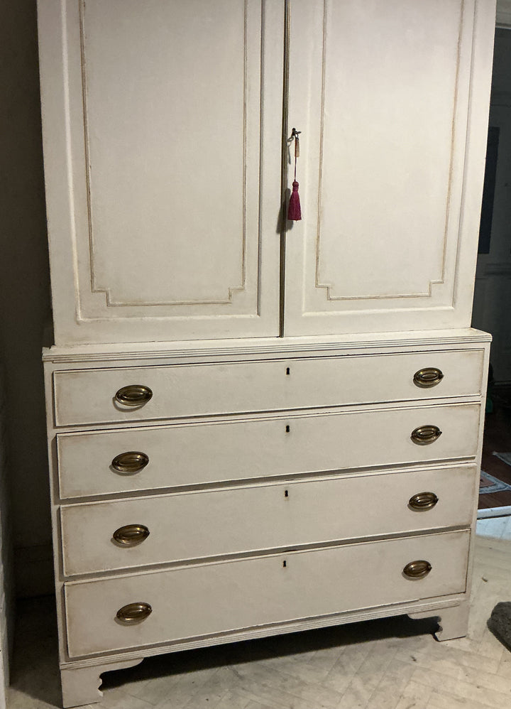 A tall, distressed white wooden cabinet with two upper doors and five drawers below, featuring brass oval handles and a small tassel keychain hanging from the center door handle