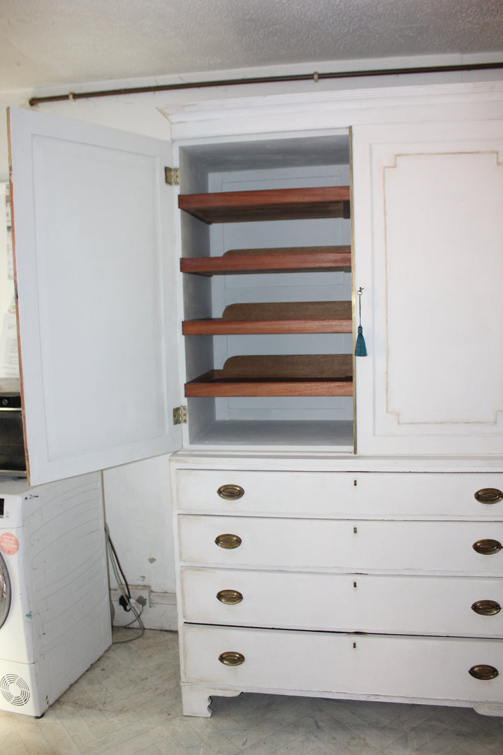A white wooden storage cabinet with an open door showing four wooden shelves inside, next to a white dresser with brass handles