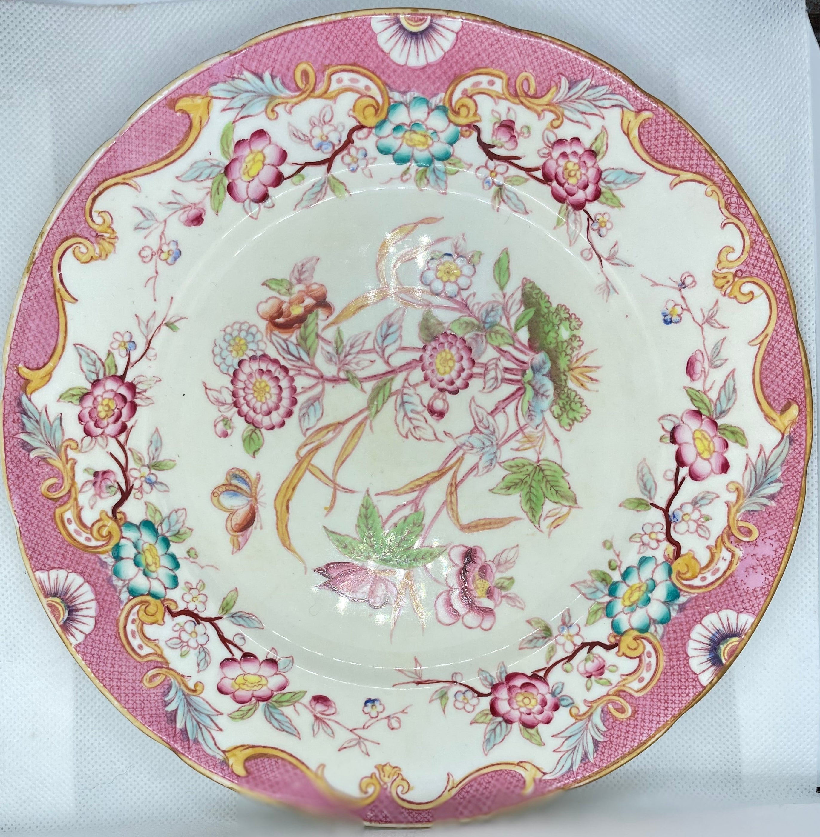 decorative ceramic plate with a pink and gold floral pattern, displayed on a white textured surface.