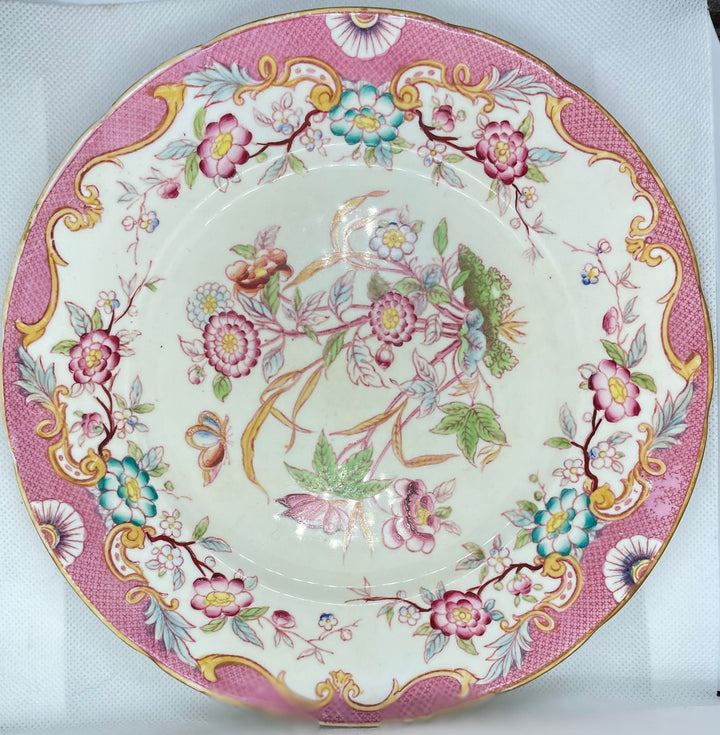 decorative ceramic plate with a pink and gold floral pattern, displayed on a white textured surface.