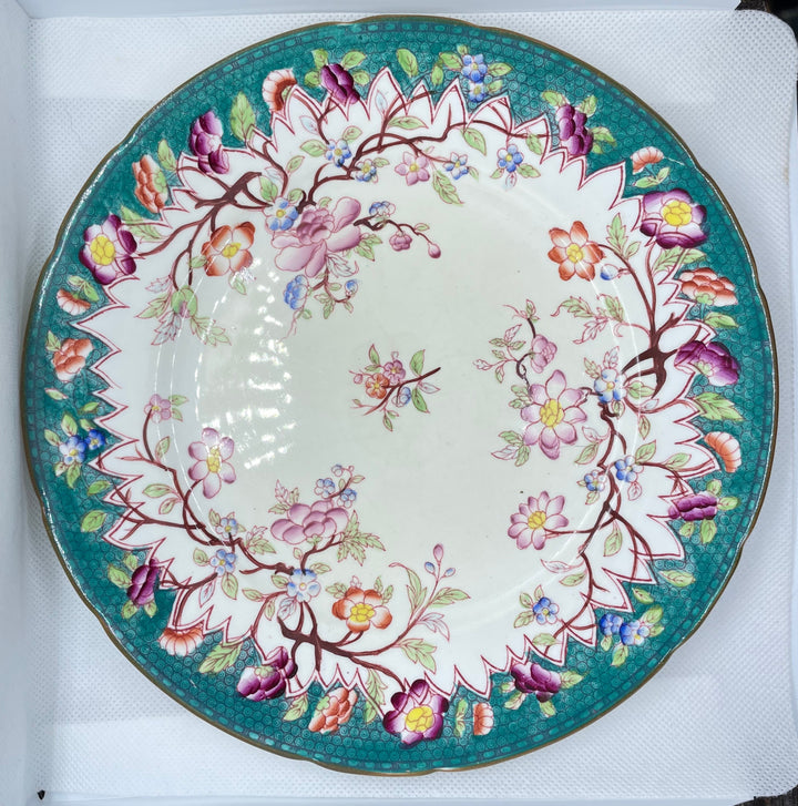 round ceramic plate with a floral pattern, featuring a teal green border, pink and purple blossoms, and a white center, displayed inside a white box.