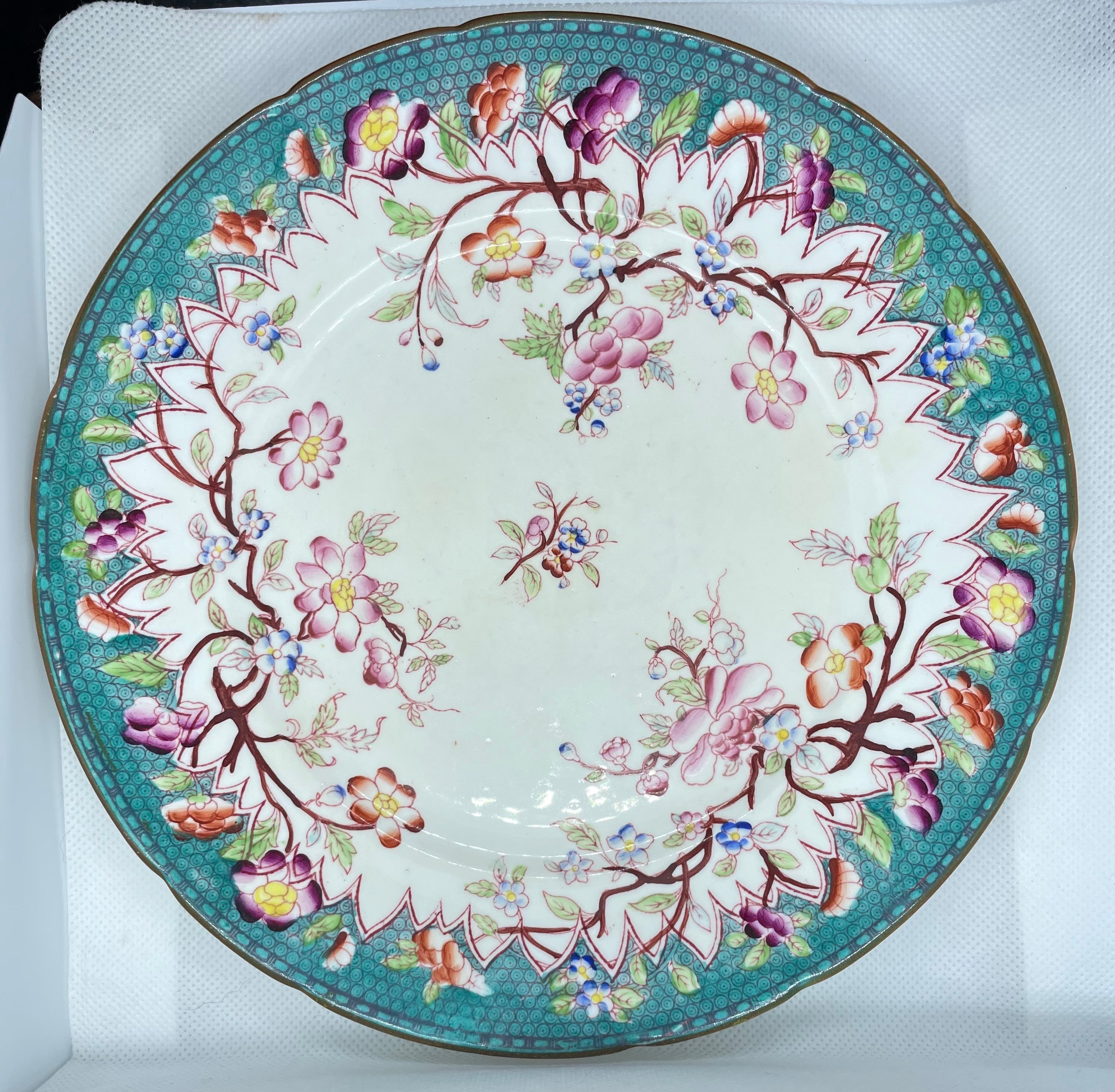An oval ceramic plate with a white center, decorated with a vibrant turquoise border and delicate pink, purple, yellow, and green floral motifs.