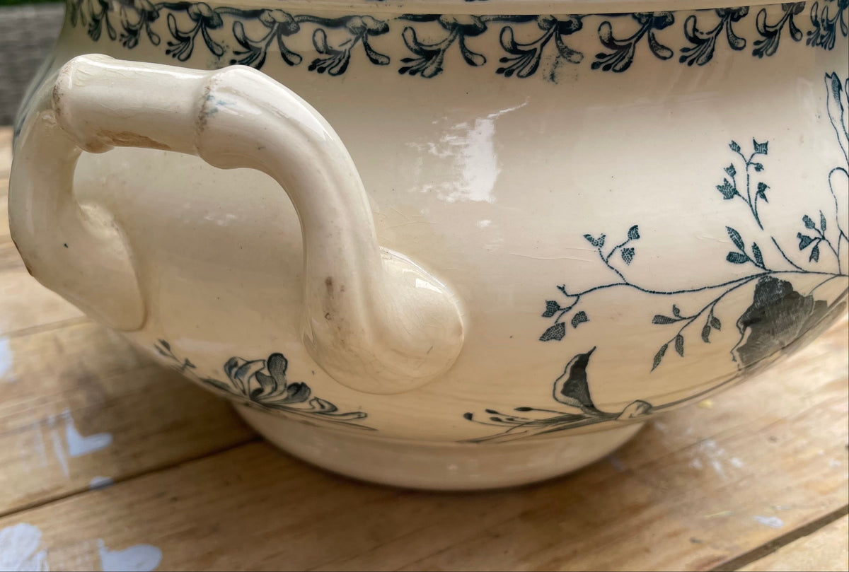 An off-white ceramic bowl with a dark blue floral pattern and a curved side handle, shown on a wooden table.
Details