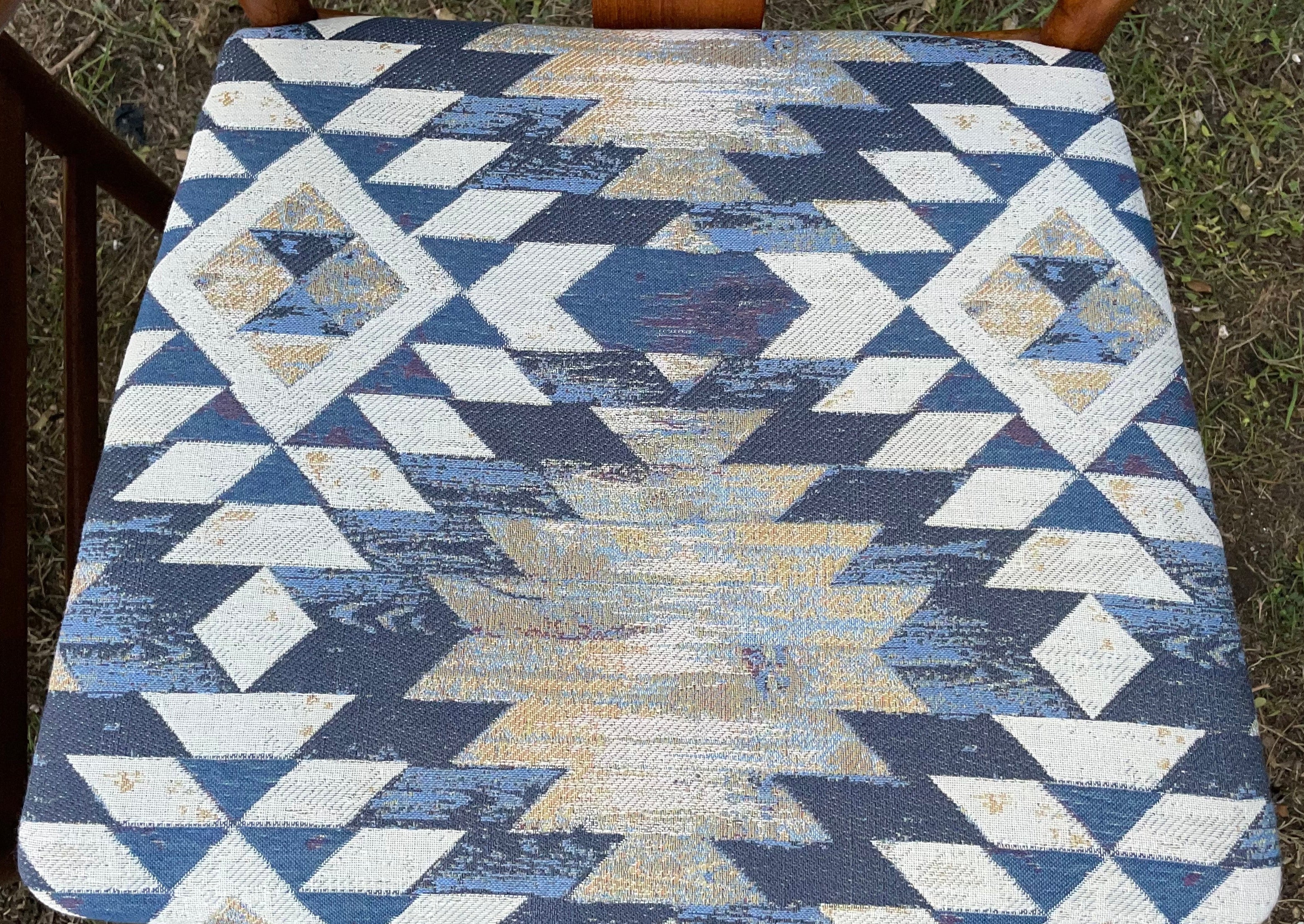 A square woven chair cushion with a Southwestern geometric pattern in navy blue, beige, and white, shown on a wooden chair outdoors.
