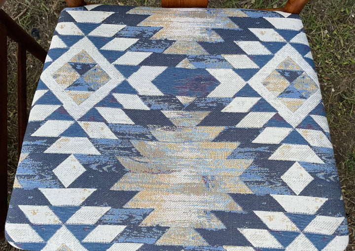 A square woven chair cushion with a Southwestern geometric pattern in navy blue, beige, and white, shown on a wooden chair outdoors.