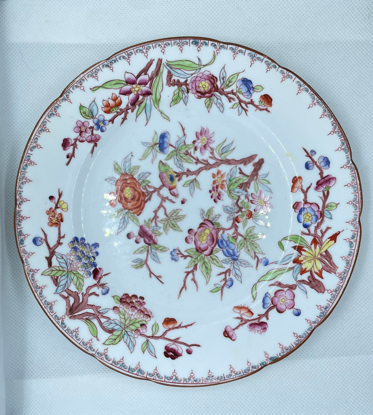 A round white porcelain plate with a colorful floral and botanical pattern, displayed inside a white textured box.
Details