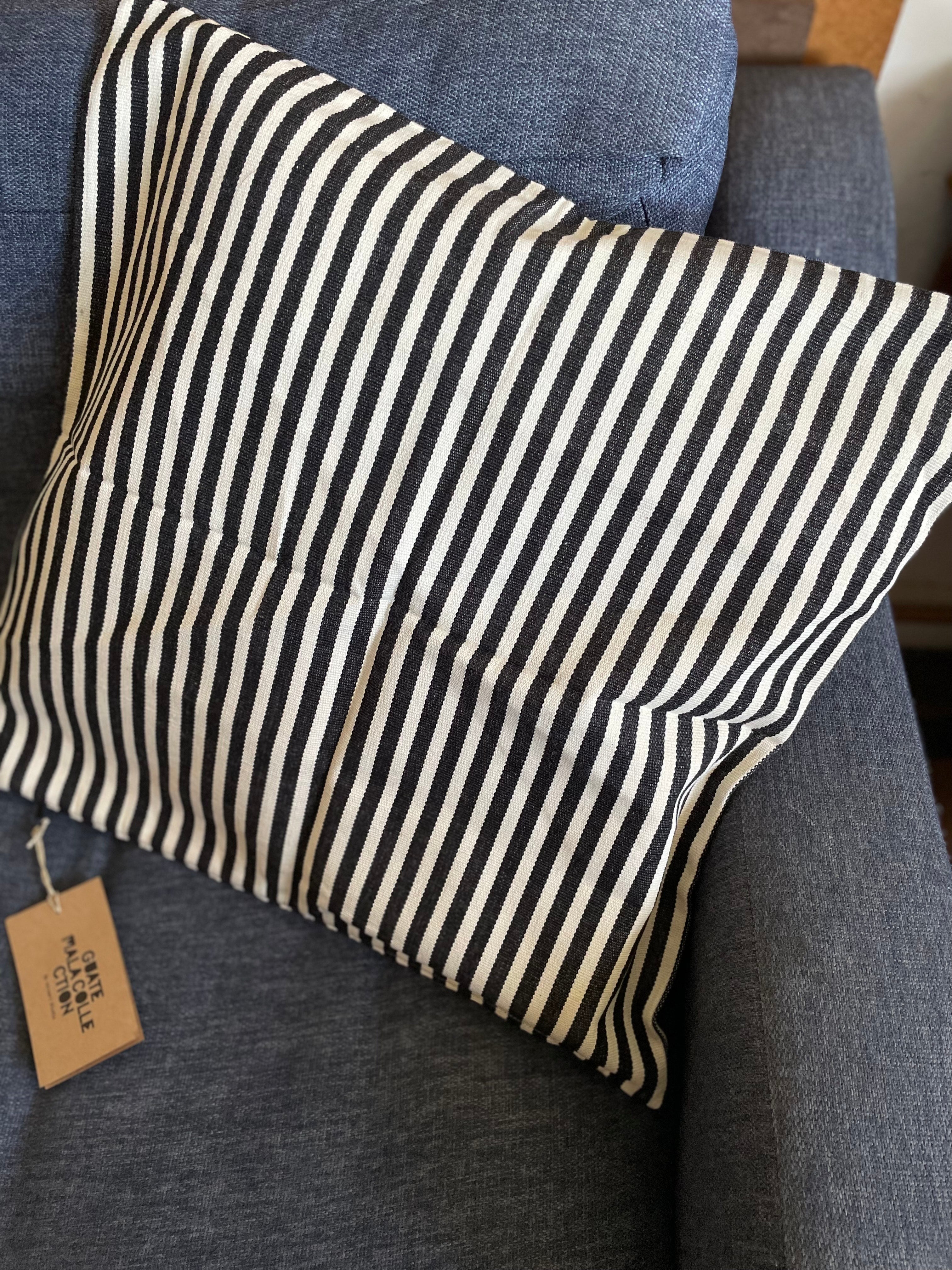 Striped pillow on a gray couch with a visible tag.