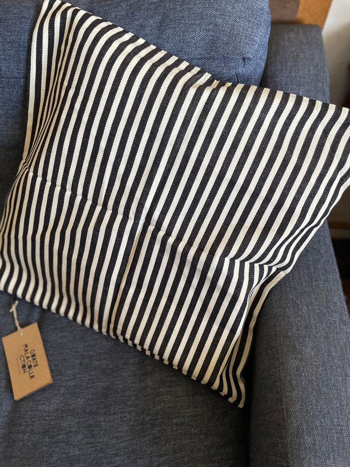 Striped pillow on a gray couch with a visible tag.