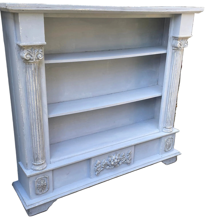 A distressed light blue painted bookcase with decorative pillars and three open shelves
