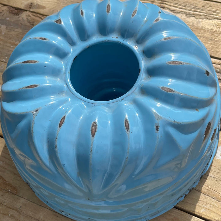A light blue glazed ceramic bundt-style cake pan with decorative ridges and small perforations, photographed on a wooden deck surface.
Details